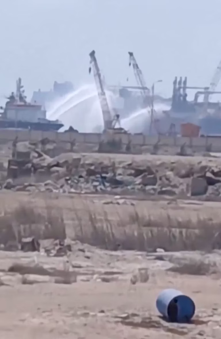 Industrial port area with smoke rising in the distance and a blue drum in the foreground