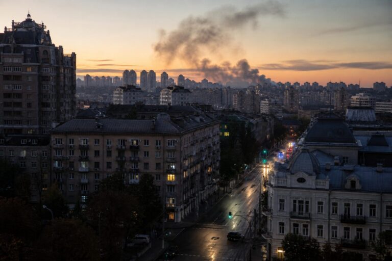 Smoke over a city skyline at dusk seen above apartment blocks and a lit street