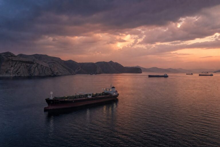 Oil tanker at anchor in a mountain-lined bay at sunset with other ships behind