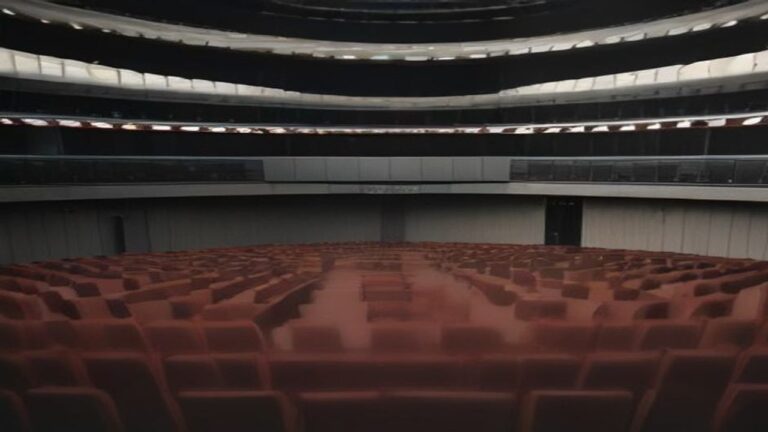 Empty parliament chamber with rows of red seats and curved balconies