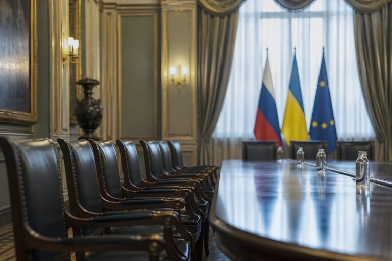 Empty meeting room with a polished table and Russian, Ukrainian and EU flags by the window
