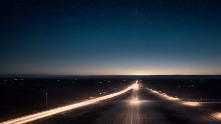 Straight road with light trails stretching across a dark landscape under a night sky
