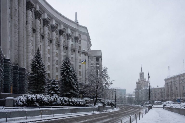 Snow-covered government building with a Ukrainian flag along a wintry city street