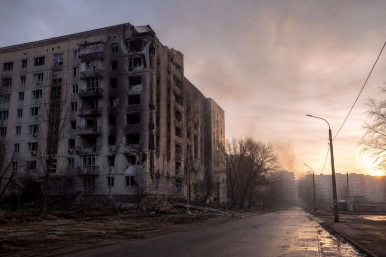 Burned-out, shell-damaged apartment block beside an empty street at sunset