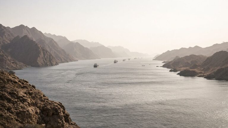 Mountain-lined sea channel with a string of cargo ships sailing through haze