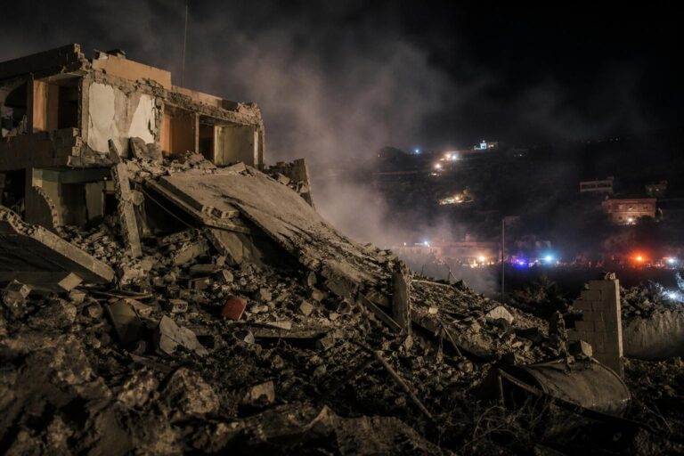 Collapsed building rubble at night with emergency lights in the background