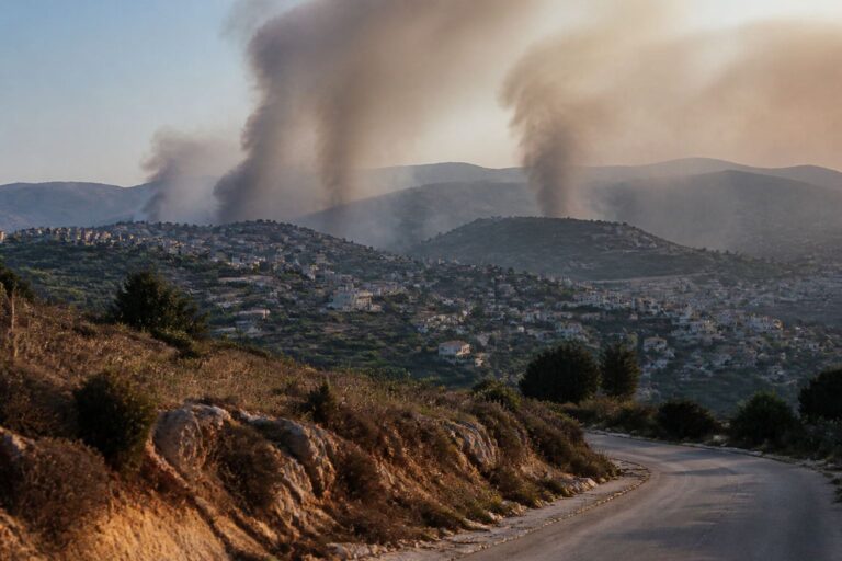 Smoke rising from hillside villages above a winding road in the hills
