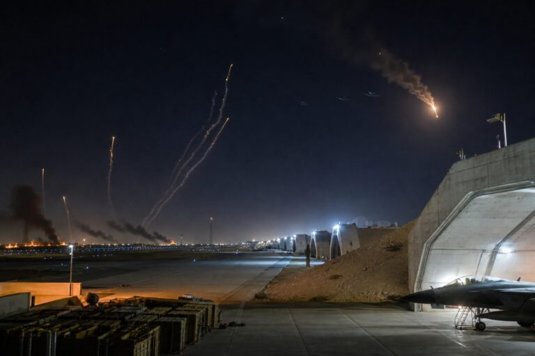 Missile and interceptor trails over an air base runway and hangar at night