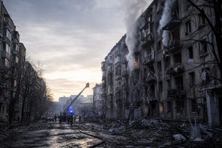 Firefighters with a ladder truck at a burning apartment block amid rubble
