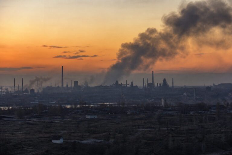 Black smoke drifting over an industrial skyline at sunset