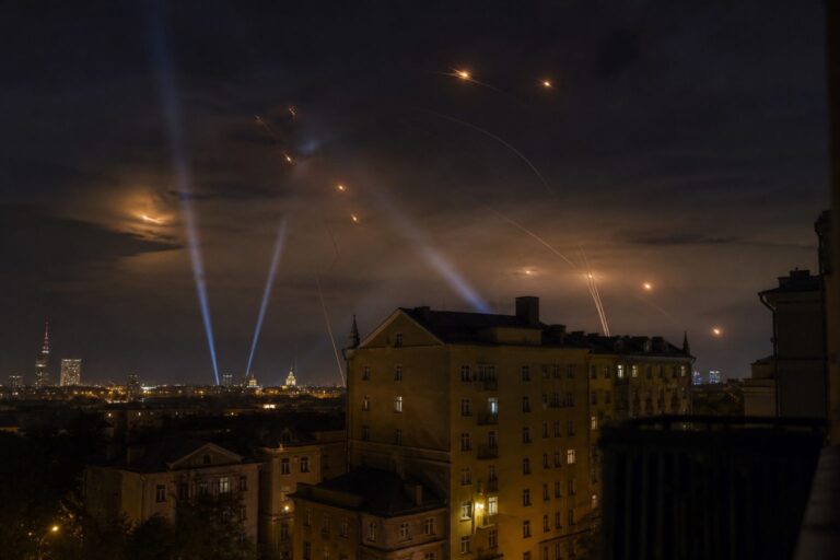 Searchlights and air-defense tracers over a city skyline at night