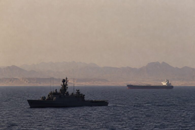 Warship and a tanker on hazy water with desert mountains behind