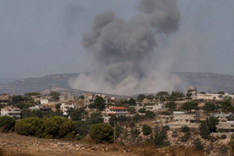 Large smoke plume rising behind a hillside village